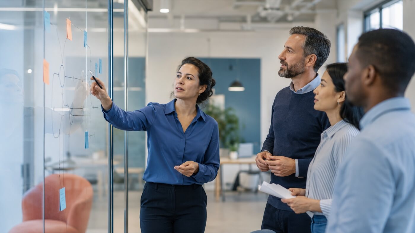 A marketer mapping out a plan on a glass wall of sticky notes with colleagues